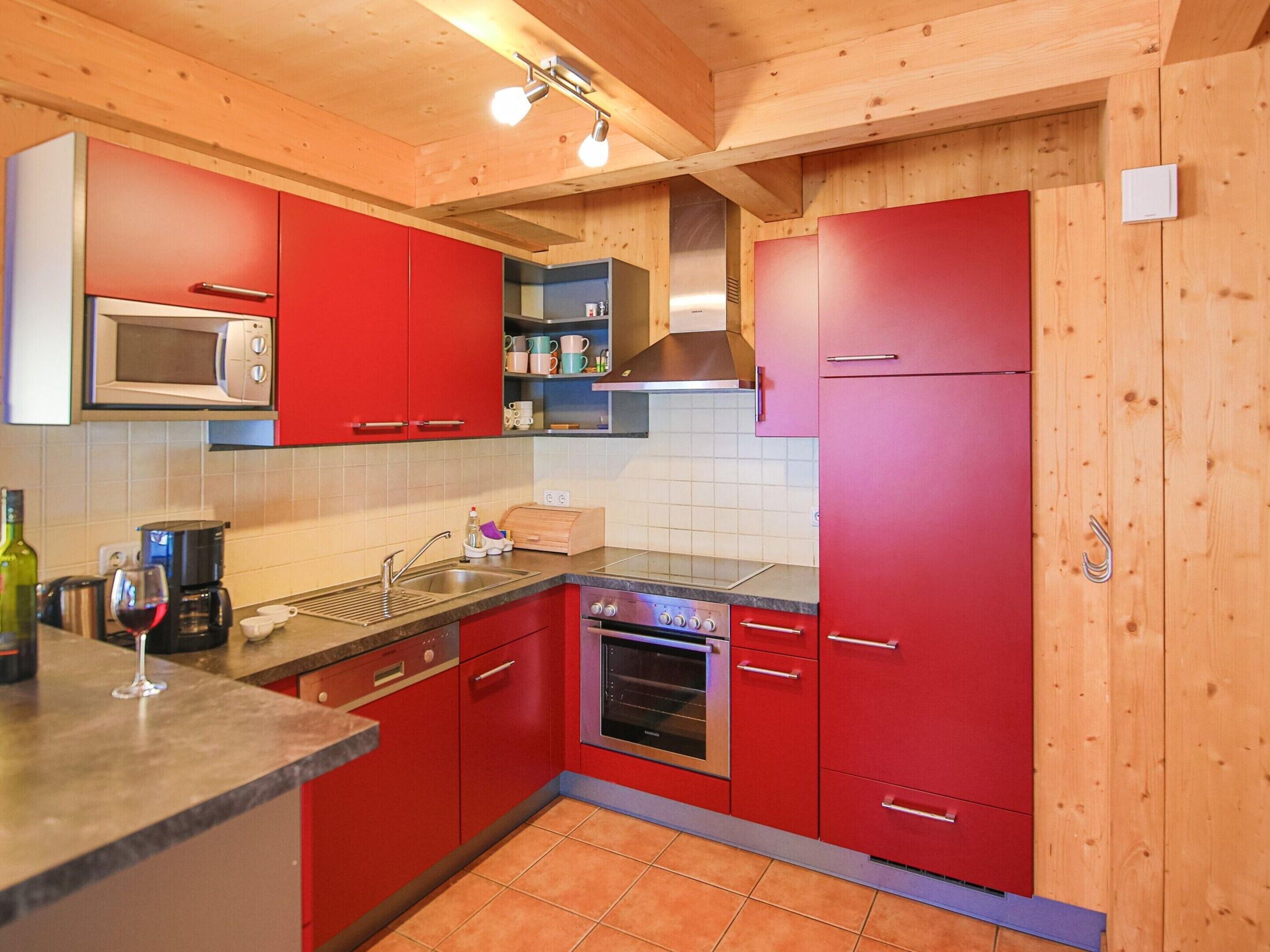 A kitchen with red cabinets, a microwave, a sink, and a stove.