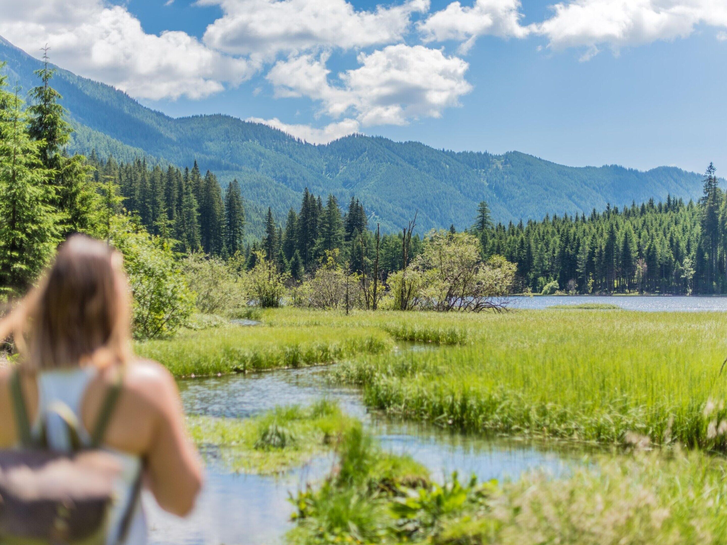 A woman sitting by a river with mountains in the background.