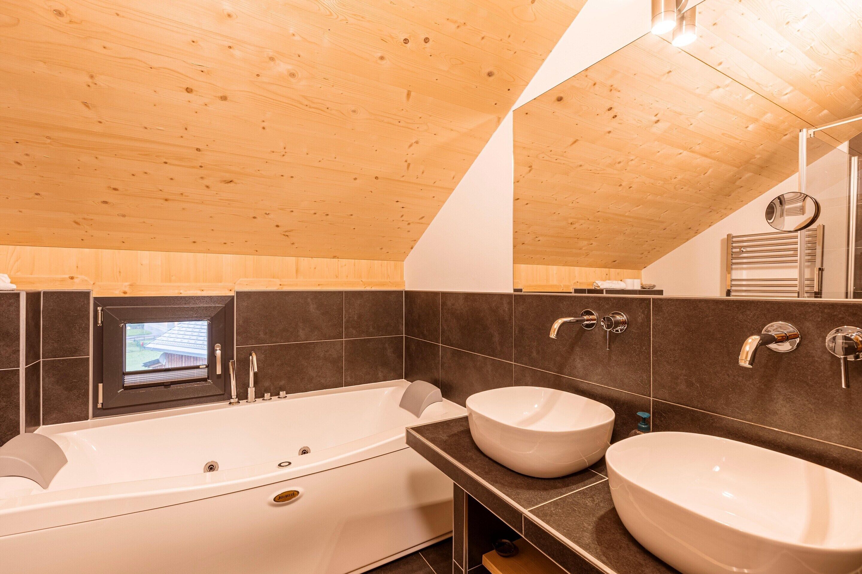 Un baño moderno con una bañera independiente, dos lavamanos y un ventanal pequeño.