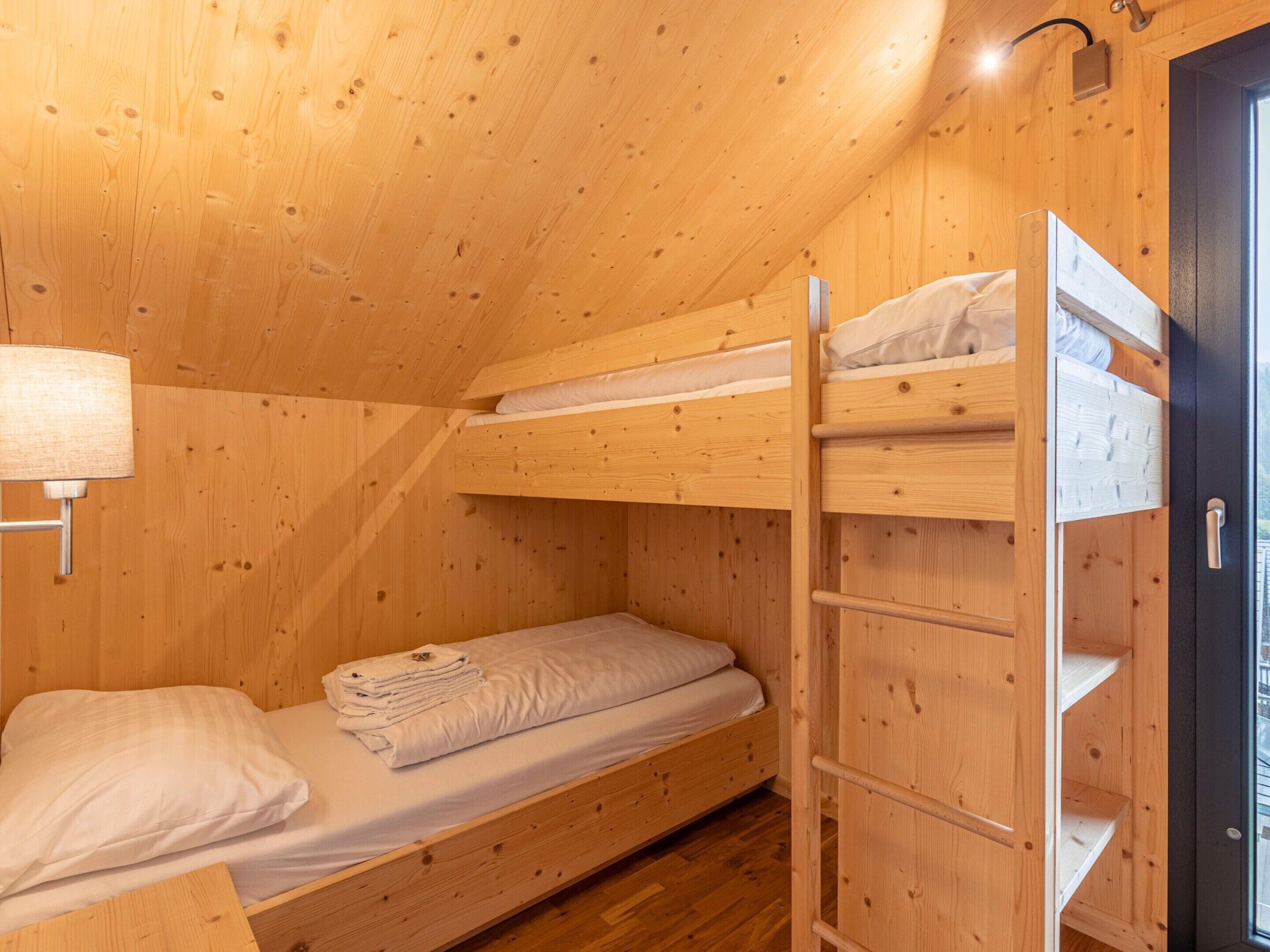 Ein kleines Holzhütten-Zimmer mit Etagenbetten, einem kleinen Nachttisch und einem Fenster.