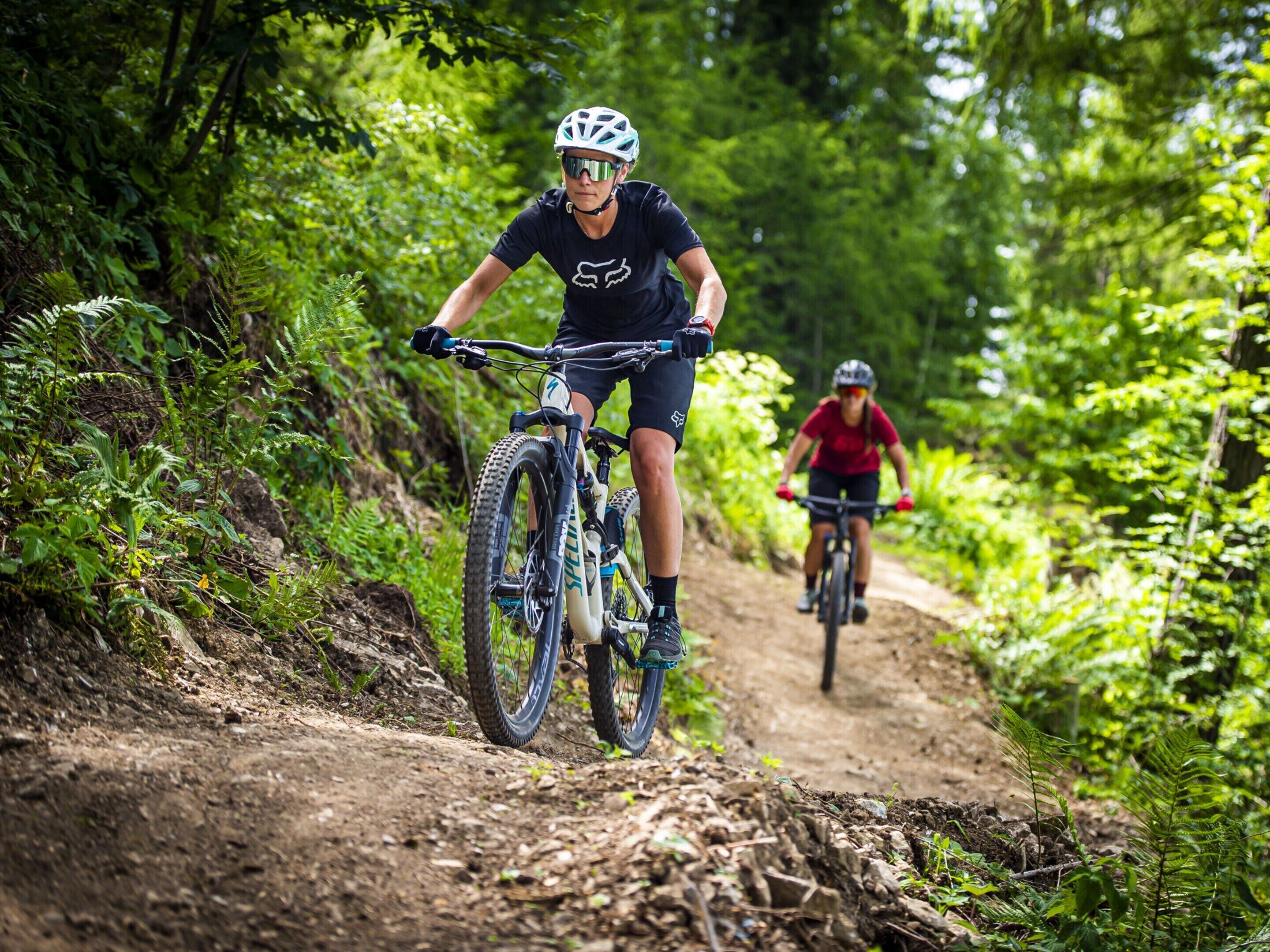 Two cyclists on a dirt trail surrounded by dense greenery.