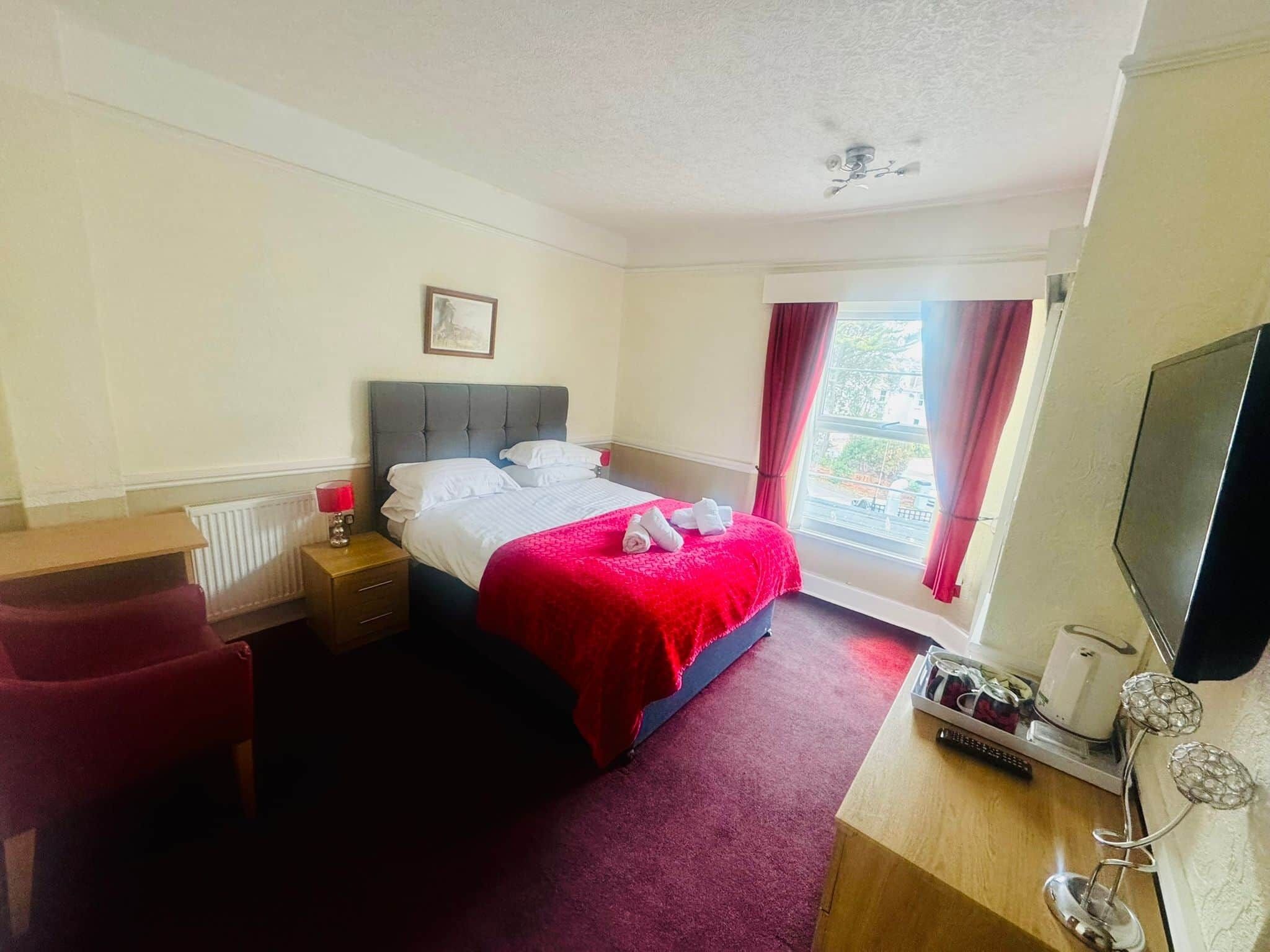 Hotelkamer met een bed, bureau, stoel, radiator, raam met gordijnen en een televisie.