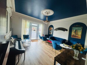 A room with a piano, blue seating, a chandelier, and a poster on the wall.