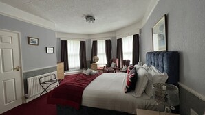 Ein Hotelzimmer mit einem ordentlich bezogenen Bett, einem Sessel, einem Schreibtisch und einem Fenster mit Vorhängen.