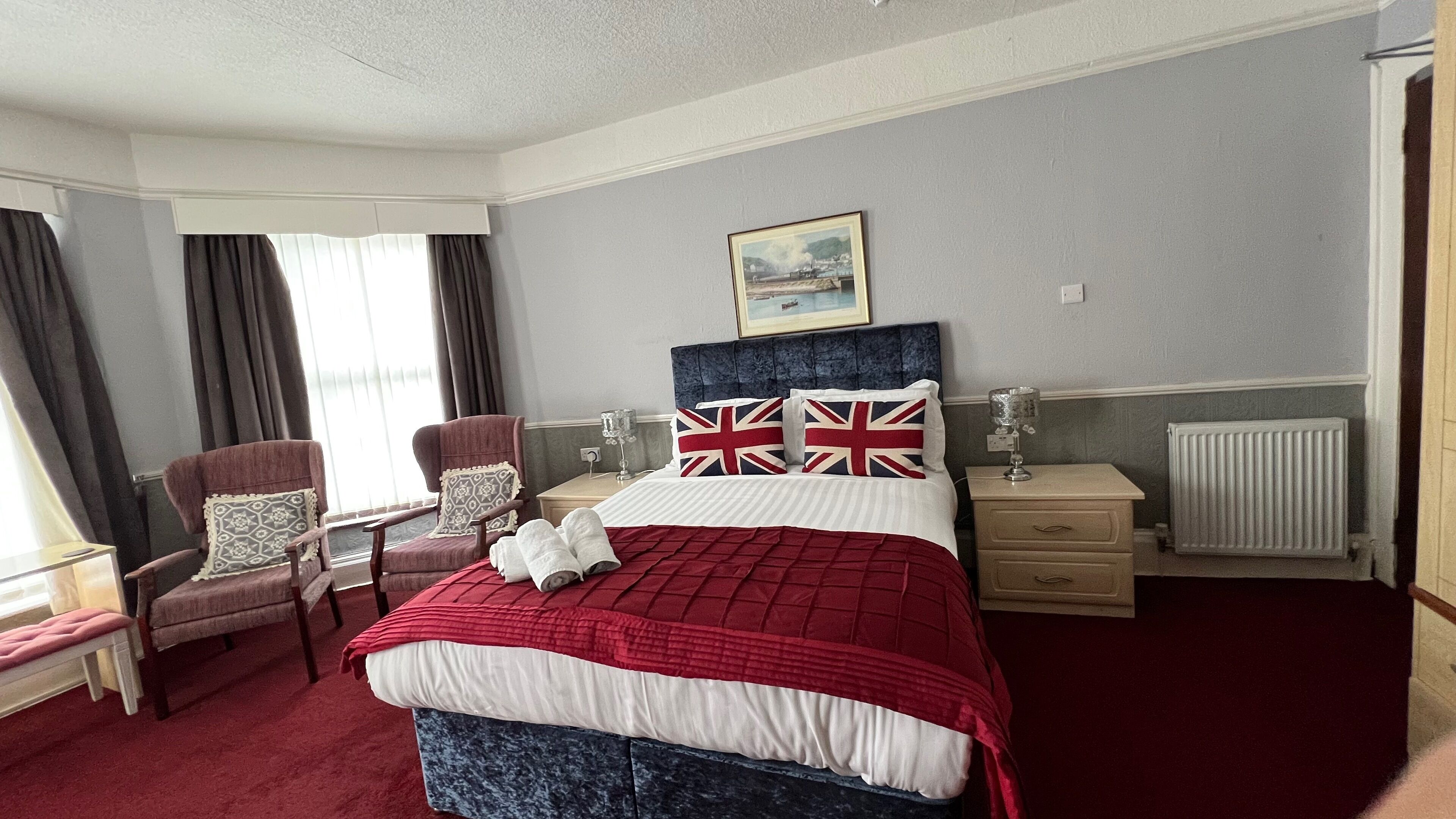 A hotel room with a bed, two armchairs, a bedside table, a lamp, and a window with curtains.