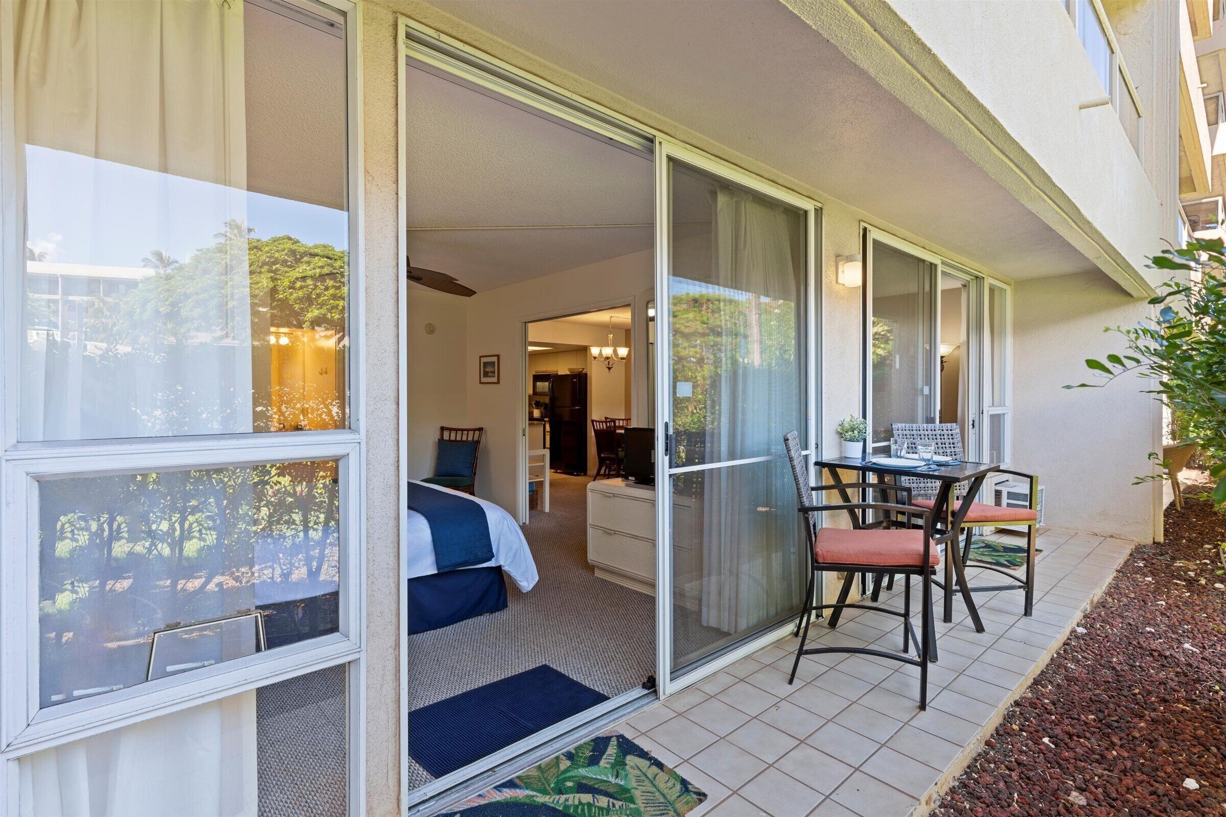 A hotel room with a bed, a desk with a chair, and a sliding glass door leading to a balcony.