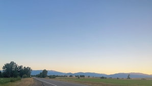 Une route de campagne bordée de champs et avec des montagnes qui se dessinent à l'horizon.