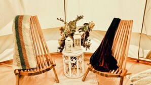 Une tente avec deux chaises en bois, une petite table sur laquelle est posée une lanterne, et un arrangement floral.