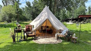 Une tente accueillante, avec un intérieur en bois, entourée d’une pelouse agrémentée d’un tapis rond et de meubles rustiques.