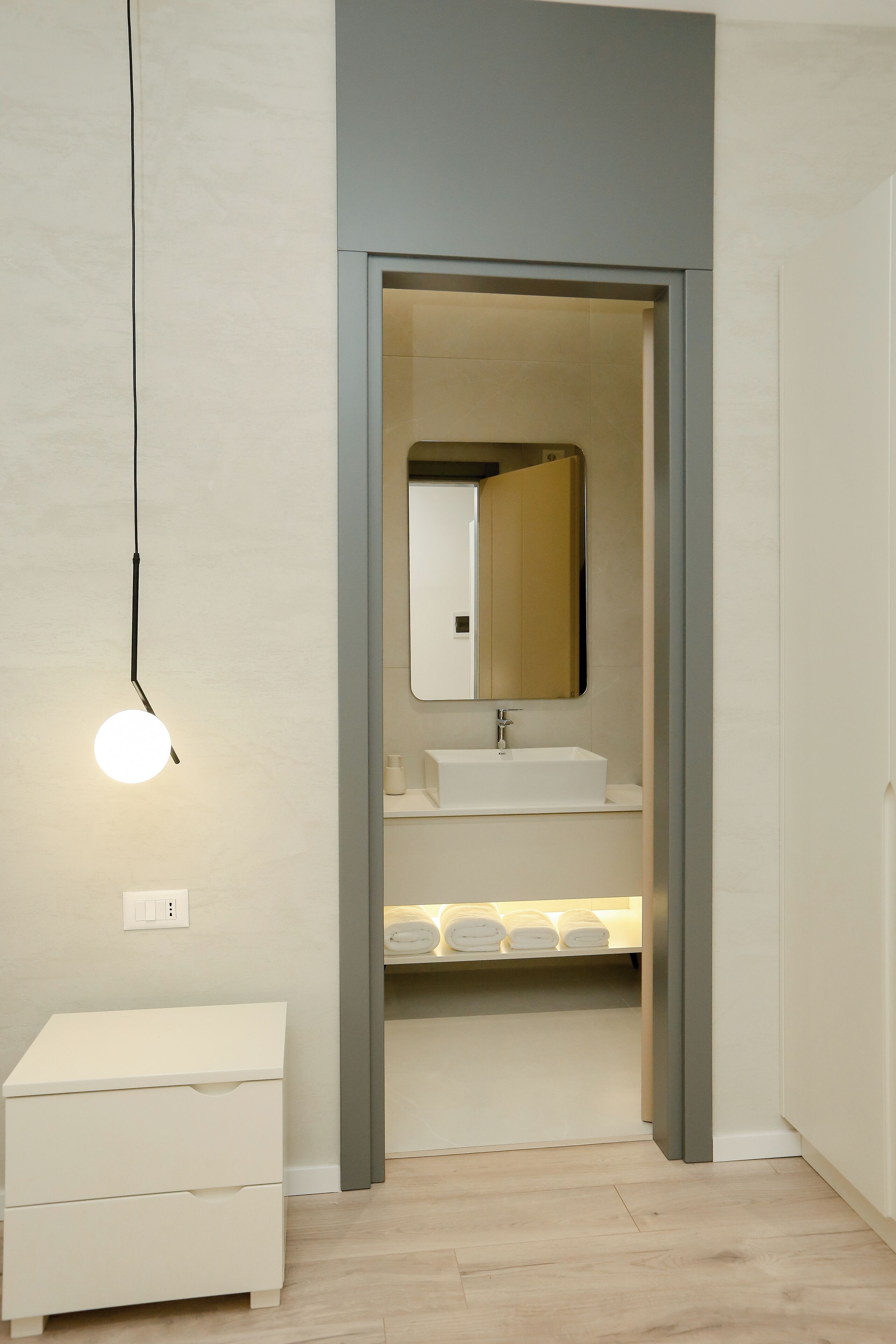 Un baño moderno con lavamanos blanco, espejo y lámpara colgante.