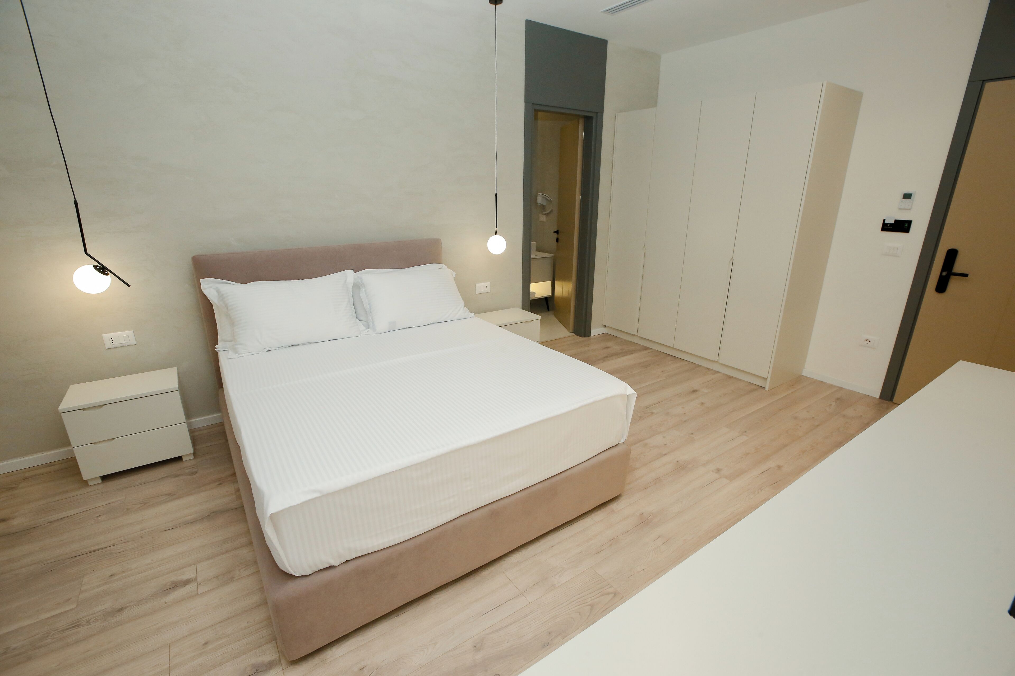 Un dormitorio moderno con una cama grande, mesitas de noche, un armario y una puerta que da al baño.
