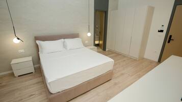 Un dormitorio moderno con una cama grande, mesitas de noche, un armario y una puerta que da al baño.
