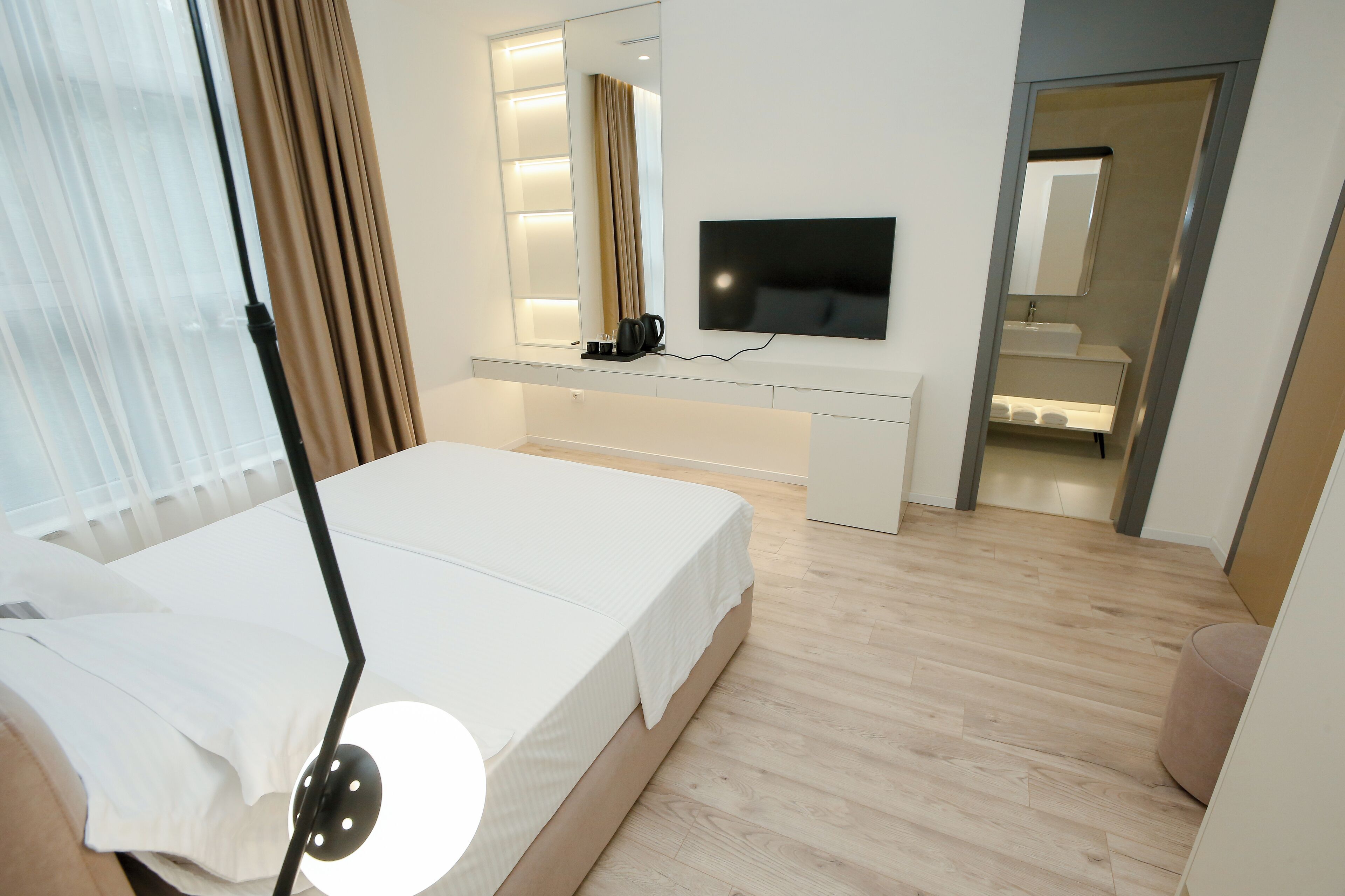 Una habitación de hotel moderna con una cama grande, un televisor de pantalla plana, una mesita de noche con cafetera y un espejo.