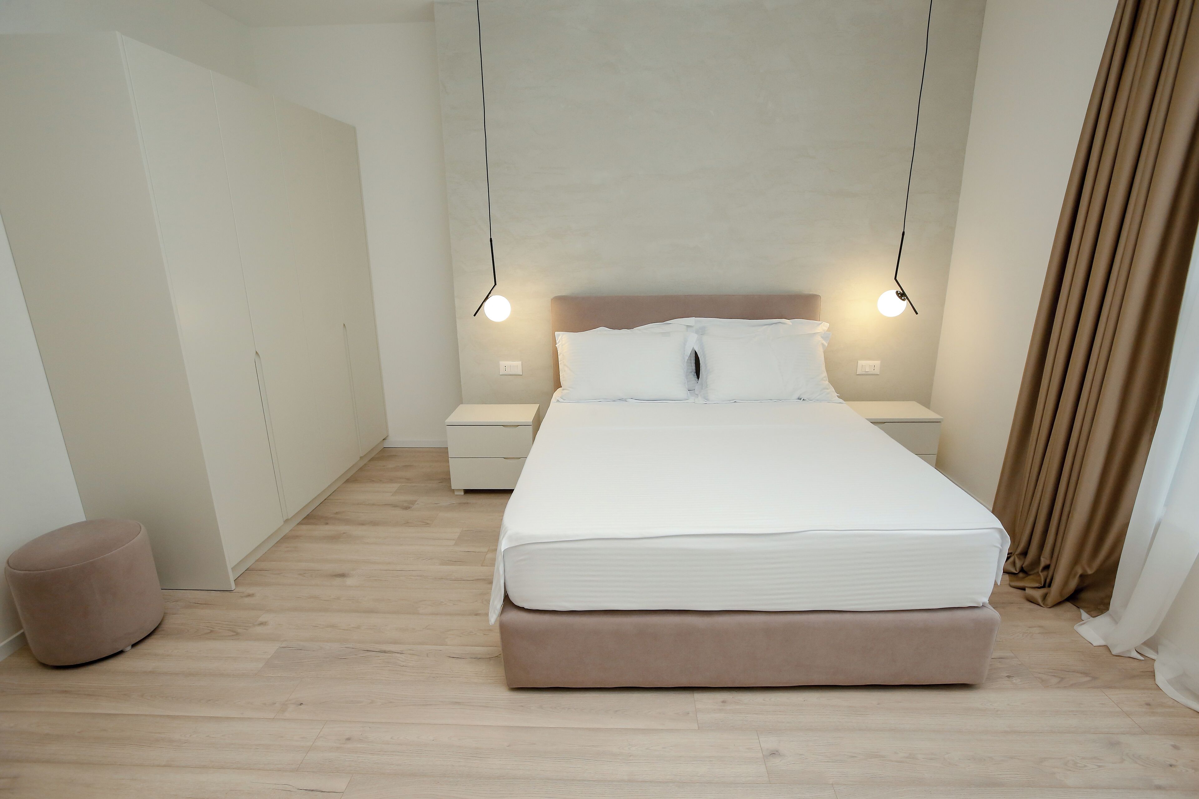 A modern bedroom with a large bed, bedside tables, and a hanging light fixture.
