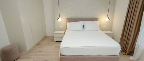 A modern bedroom with a large bed, bedside tables, and a hanging light fixture.