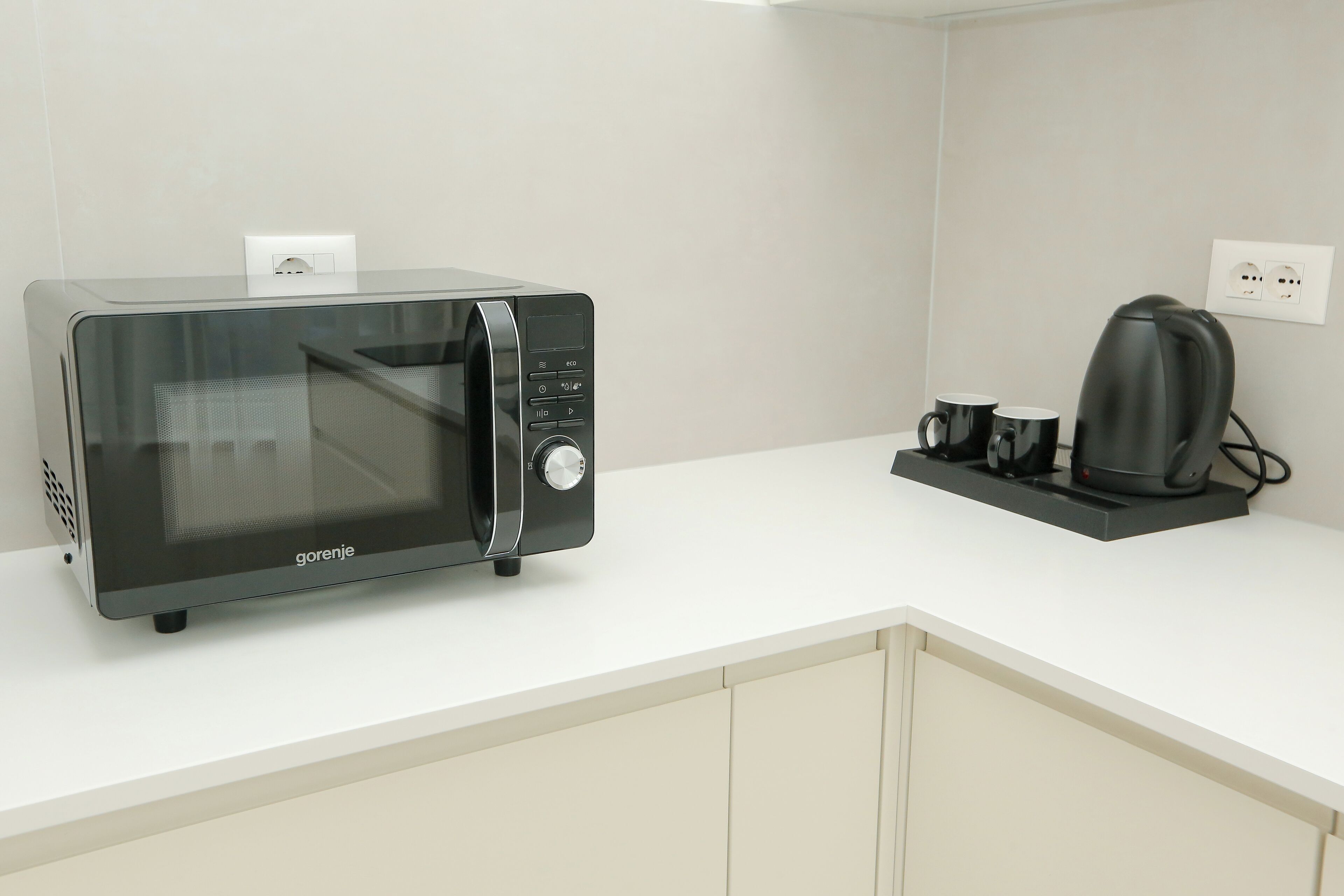 A kitchen with a modern microwave, a coffee maker, and a power outlet on the counter.