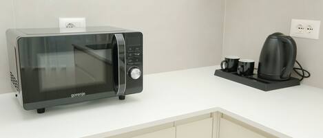 A kitchen with a modern microwave, a coffee maker, and a power outlet on the counter.