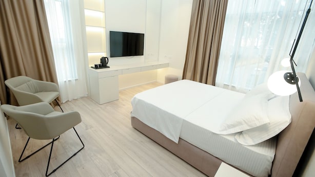 Une chambre d’hôtel moderne équipée d’un lit, d’un bureau avec un téléviseur à écran plat, d’une chaise et d’une lampe.