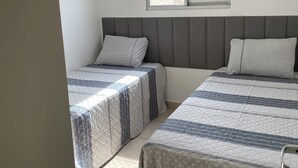 A bedroom with two beds, a window with blinds, and a tiled floor.
