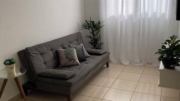 Una sala de estar con un sofá gris, una mesita con una planta y otra planta en un pedestal.
