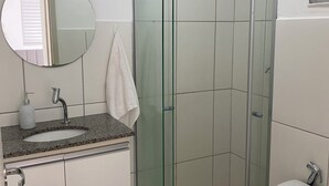 A bathroom with a glass-enclosed shower, a sink with a faucet, a toilet, and a mirror on the wall.