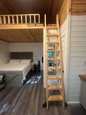 Une chambre avec un lit en mezzanine, une échelle en bois, une table de chevet et une commode.