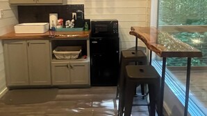 Cocina compacta con armarios de madera, cafetera, microondas y ventana con vistas a un bosque.