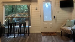 Interior acogedor de una cabaña con paredes de madera, un comedor con taburetes, un sofá y un televisor montado en la pared.