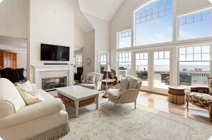 Un salon spacieux doté d’une cheminée, d’un téléviseur et de grandes fenêtres offrant une vue sur l’extérieur.