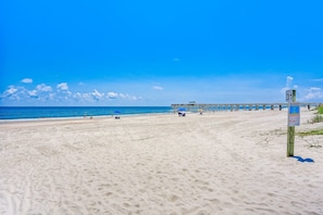 A beach with a pier extending into the ocean, a signpost with route information, and a clear blue sky. - 3 Sea Castles - Townhome with Peekaboo Ocean Views Just Steps to the Water (Fernandina Beach)