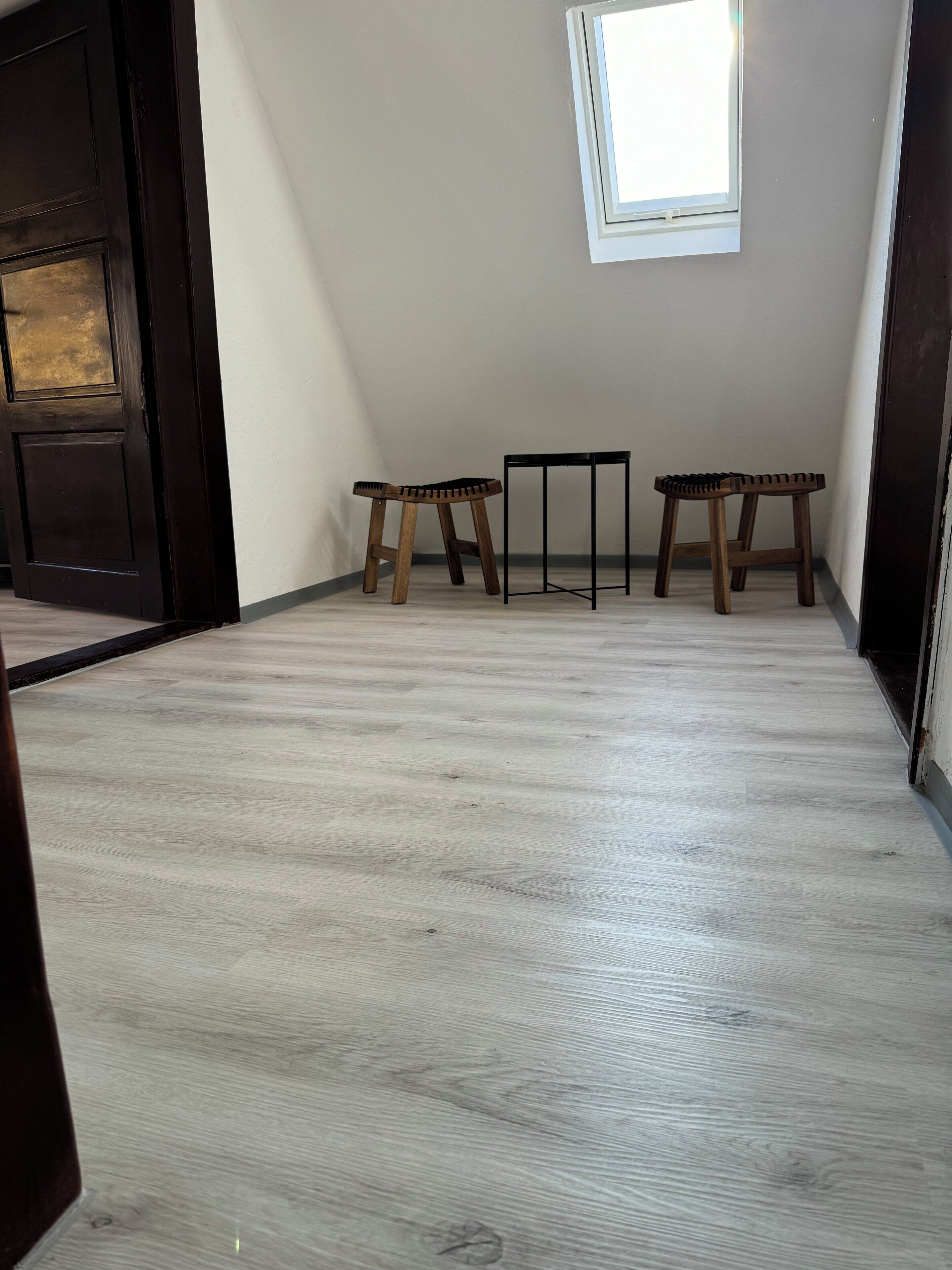 A room with a light wooden floor, a black door, a window, and two wooden stools.