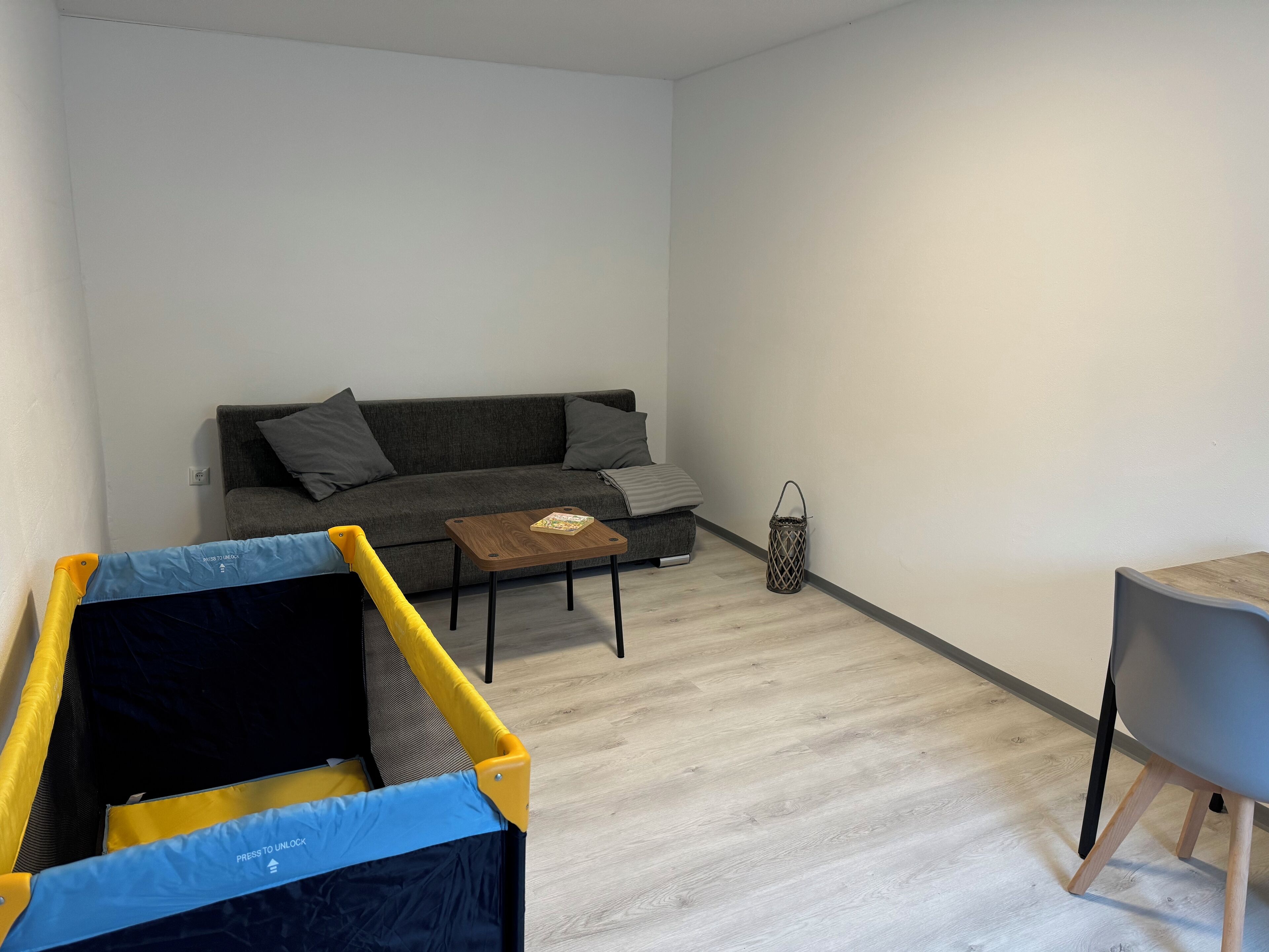 Ein Wohnzimmer mit grauem Sofa, einem kleinen Holztisch und einem Spielbereich.