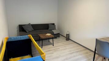 Ein Wohnzimmer mit grauem Sofa, einem kleinen Holztisch und einem Spielbereich.