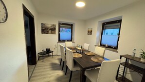 Een eetgedeelte met een lange tafel, witte stoelen en een bijzettafeltje.