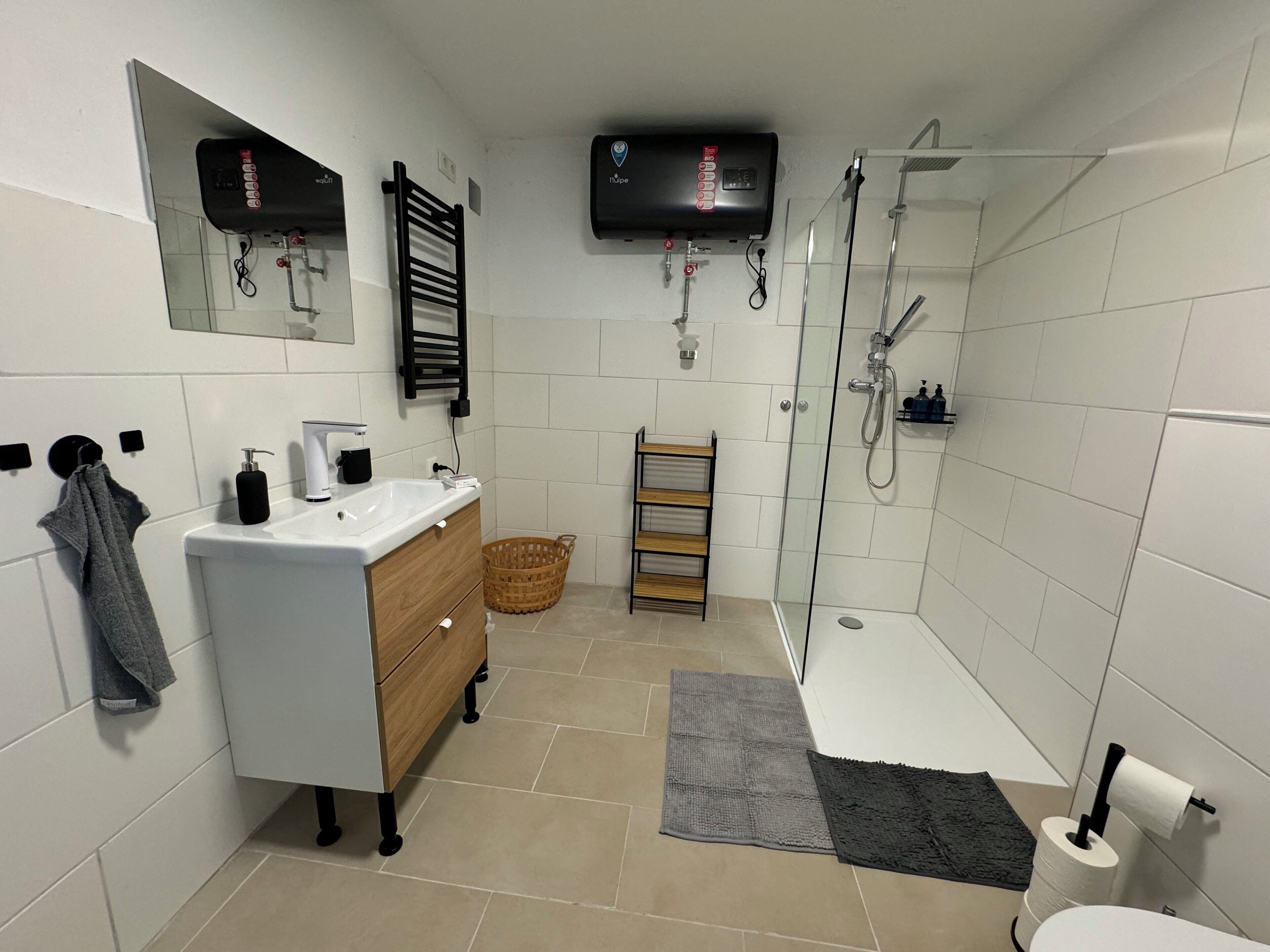 Une salle de bain moderne équipée d’un lavabo, d’un miroir, d’un porte-serviettes, d’une douche et de toilettes.