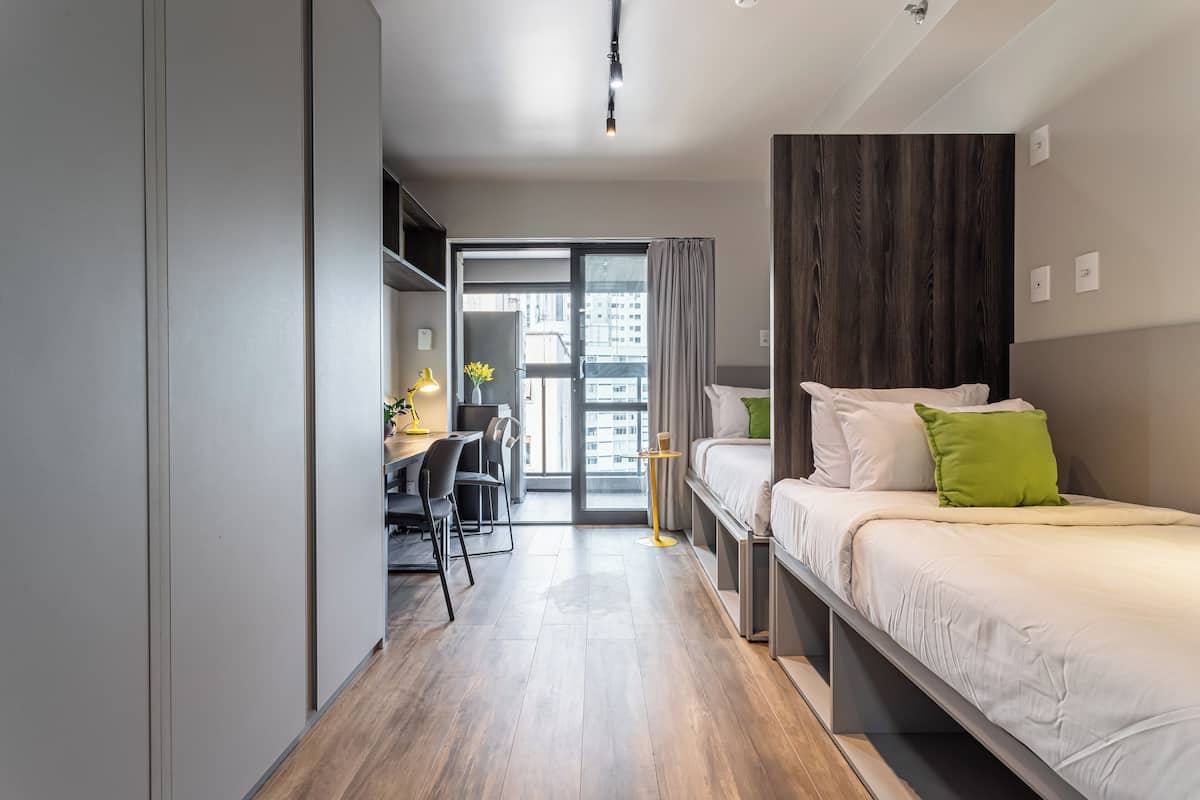 A modern hotel room with a bed, desk, chair, and a view through a glass door.