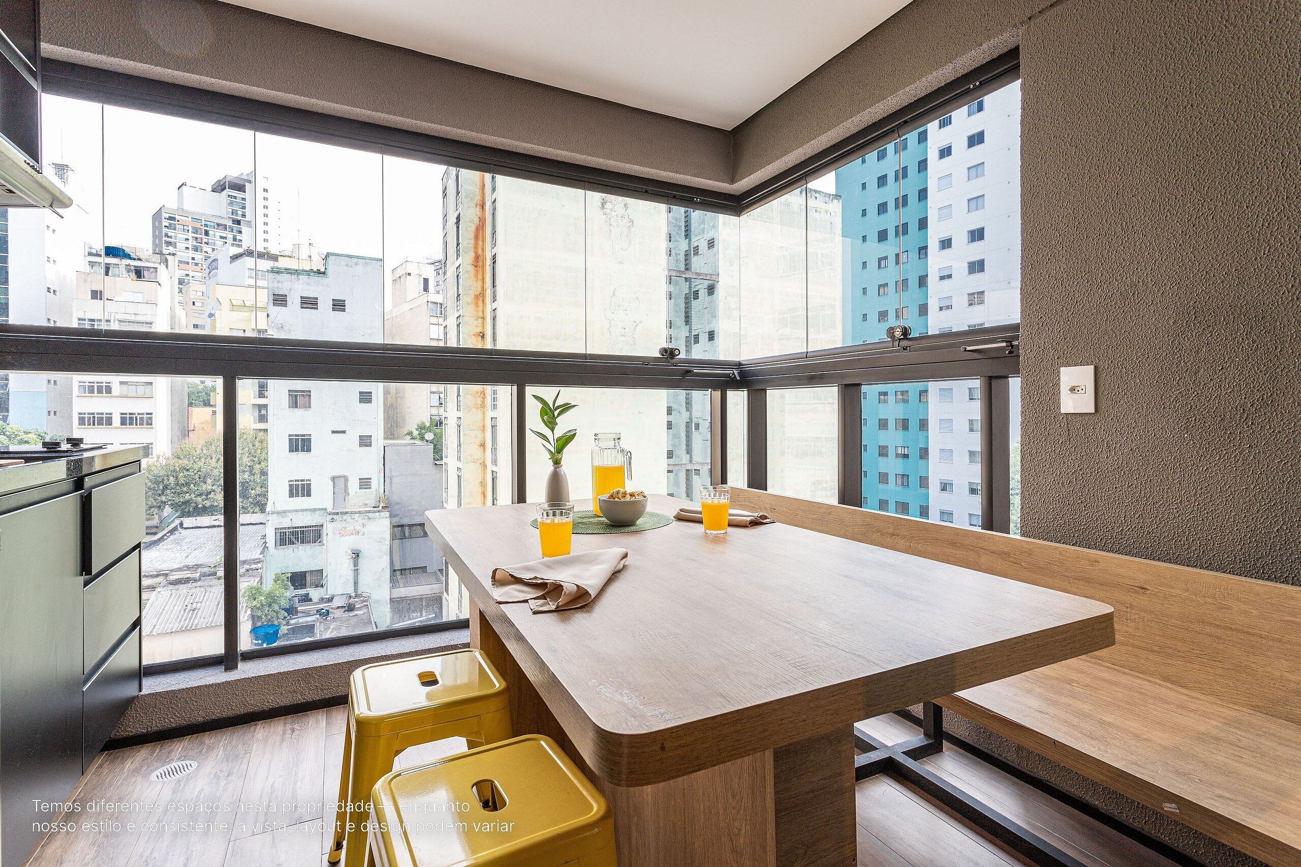 A modern kitchen with a large window, a wooden dining table, and a yellow stool.