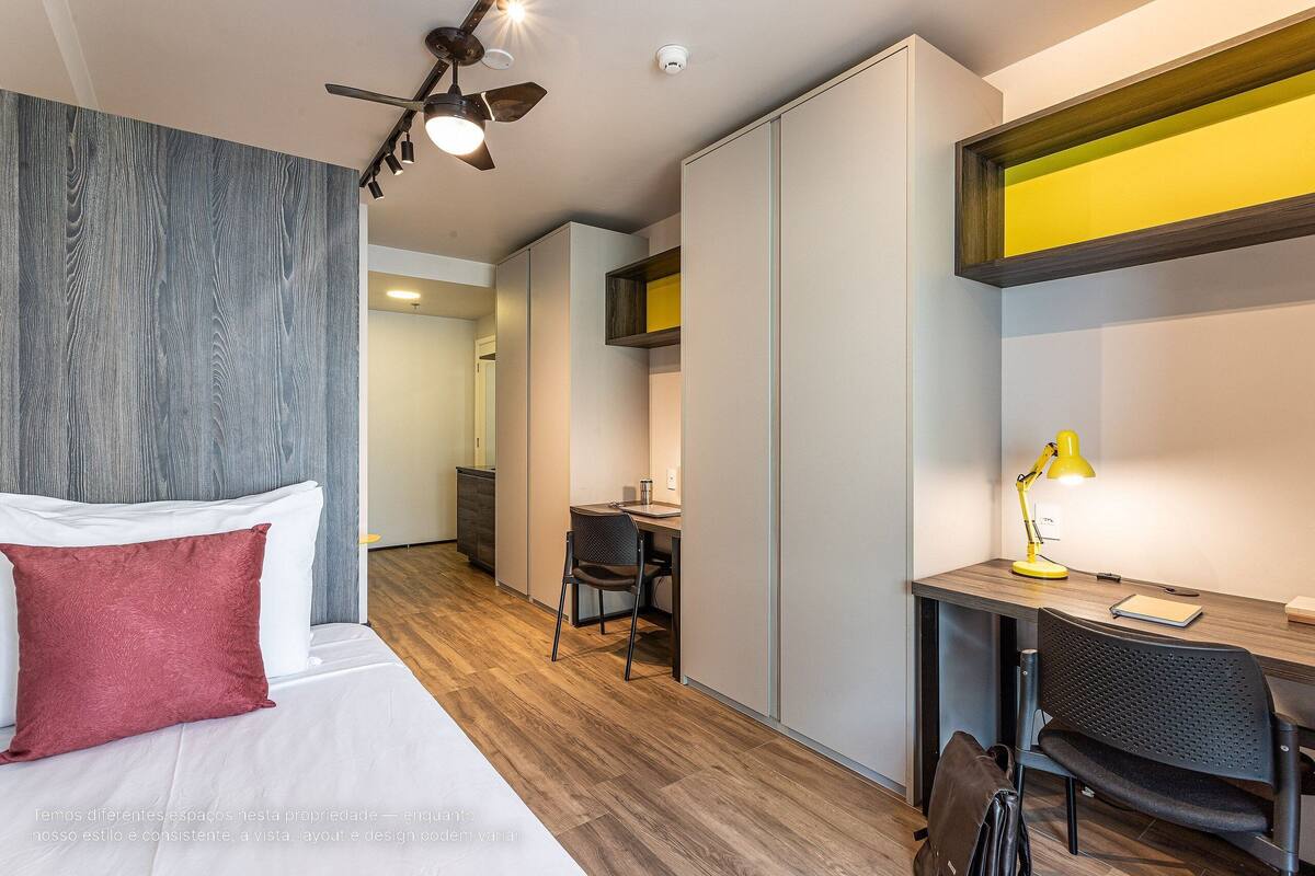 A hotel room with a bed, desk, chair, and a ceiling fan.