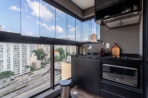 A modern kitchen with a large window, a built-in oven, and a view of the cityscape. - Share Consolação by Viva - Prédio completo na Consolação com piscina no rooftop próx ao Mackenzie (São Paulo)