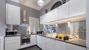 Une cuisine moderne avec des meubles blancs, un four encastré, un micro-ondes et une grande fenêtre au-dessus de l’évier.