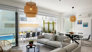 A modern living room with a sofa, coffee table, and dining area. There is a pool visible through the glass doors. - Protaras Bay View Villa 11 (Paralimni)