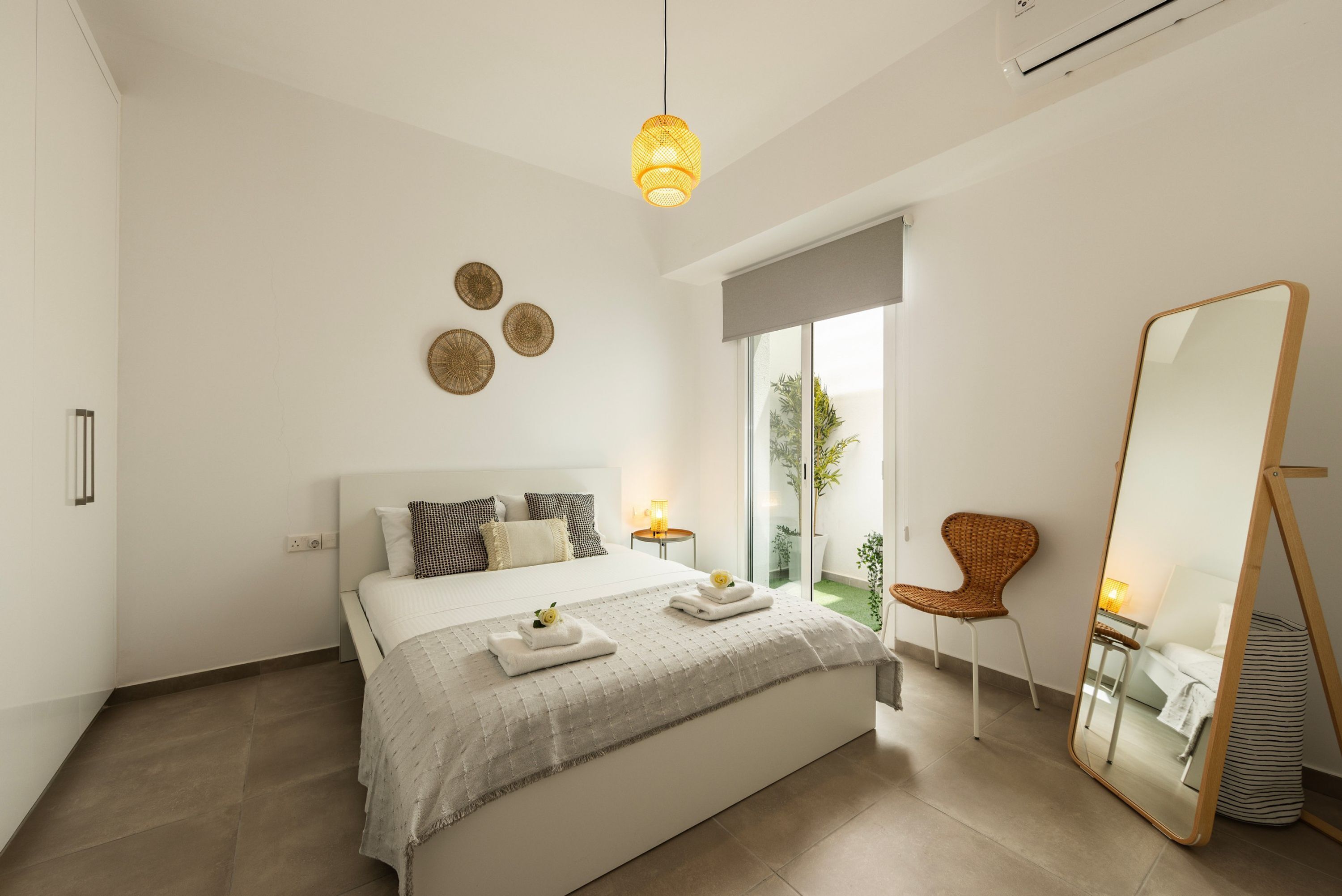 A modern bedroom with a large bed, bedside lamps, a mirror, and a view of the outdoors.