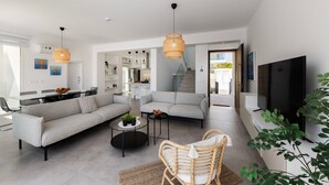 A modern living room with a grey sofa, a wicker chair, and a round coffee table. There is a television and a large window providing natural light. - Protaras Bay View Villa 11 (Paralimni)