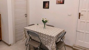 A dining area with a table set for two, a vase with flowers, and two framed pictures on the wall.