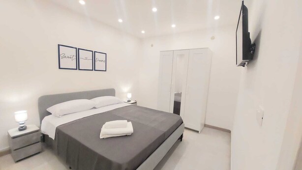 A neatly arranged bedroom with a bed, bedside tables, a wardrobe, and a TV mounted on the wall.