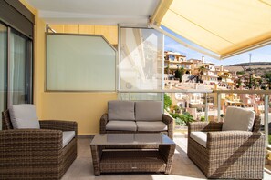 A balcony with wicker furniture, a glass table, and a view of a residential area. - Sea View Terrace Apartment Cullera (Cullera)