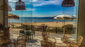 Een restaurant aan het strand met rieten meubels en parasols, met uitzicht op een strand en oceaan.