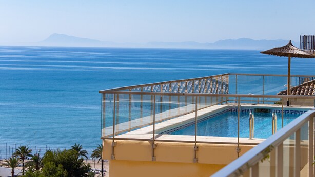 Ein Pool mit Glasgeländer, der auf einen Strand und das Meer blickt.