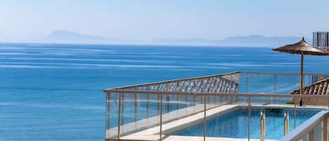 A pool with a glass balustrade overlooking a beach and the sea.