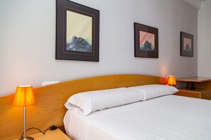 A hotel room with a bed, two bedside lamps, and three framed pictures on the wall.